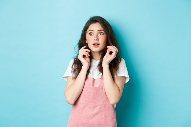 Porträt eines verängstigten, schüchternen Mädchens in Sommerkleidung, das verängstigt auf das Kopierraumbanner schaut, von etwas Beängstigendem springt und vor blauem Hintergrund steht.