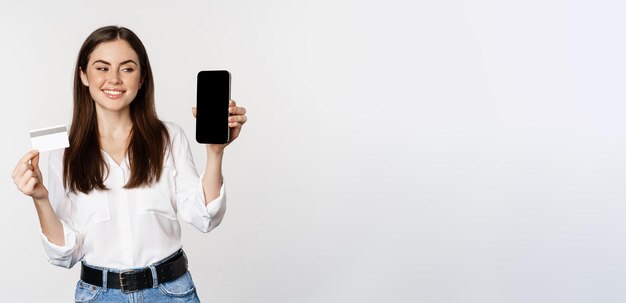 Porträt eines weiblichen Modells, das eine Kreditkarte mit Smartphone-Bildschirm zeigt, auf dem eine Anwendung empfohlen wird