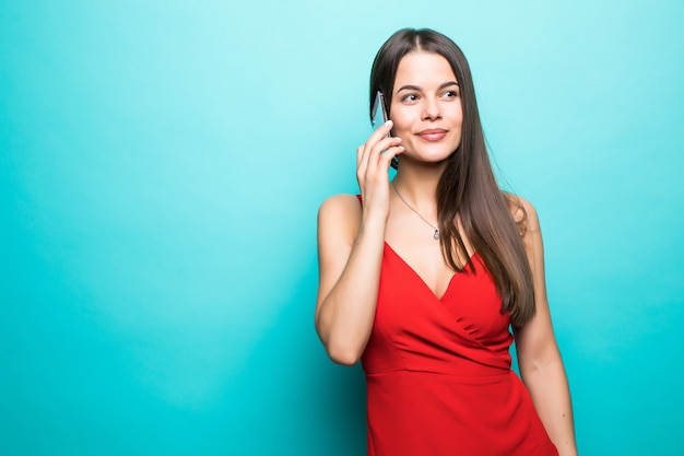 Porträt eines ziemlich freudigen Mädchens im roten Kleid, das auf Handy lokalisiert über blauer Wand spricht