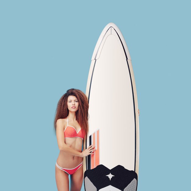 Porträt exotisches Mädchen, das mit Surfbrett aufwirft