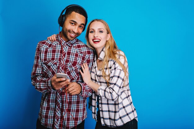 Porträt freudiges Paar der ansprechenden jungen Frau mit den langen blonden Haaren, die Spaß zusammen mit dem gutaussehenden Kerl haben, der Musik über Kopfhörer hört. Fröhliche Stimmung, lächelnd.