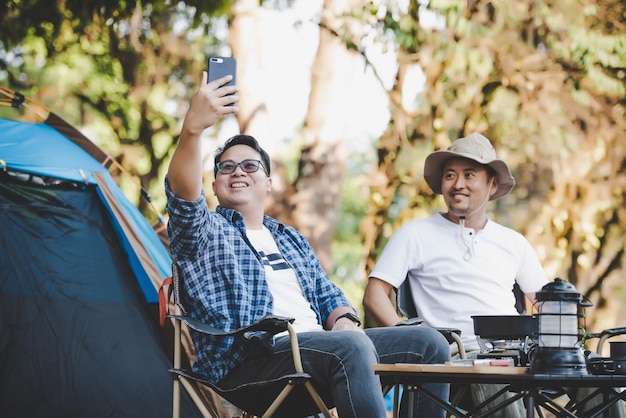 Porträt glücklicher asiatischer Mann Freunde Einen Videoanruf mit Smartphone auf dem Campingplatz machen Kochset Vorderboden Kochen im Freien Reisen Camping Lifestyle-Konzept