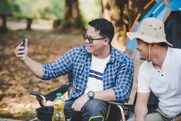 Porträt glücklicher asiatischer Mann Freunde Einen Videoanruf mit Smartphone auf dem Campingplatz machen Kochset Vorderboden Kochen im Freien Reisen Camping Lifestyle-Konzept