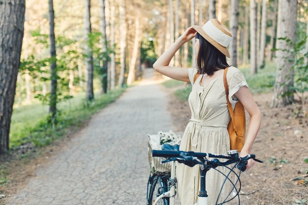 Porträt im Freien des attraktiven jungen Brunette in einem Hut auf einem Fahrrad.