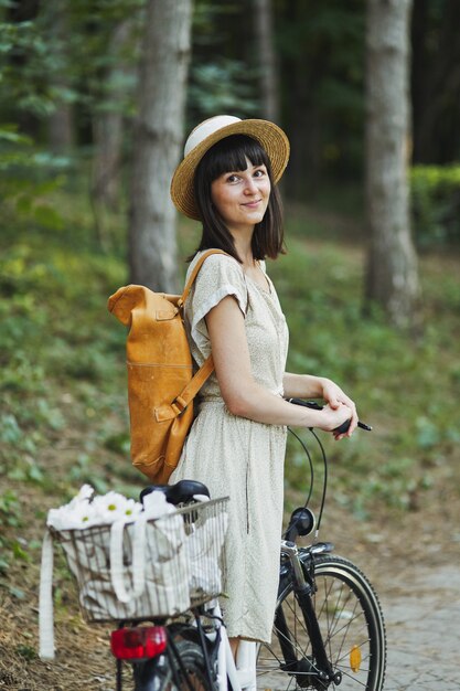 Porträt im Freien des attraktiven jungen Brunette in einem Hut auf einem Fahrrad.