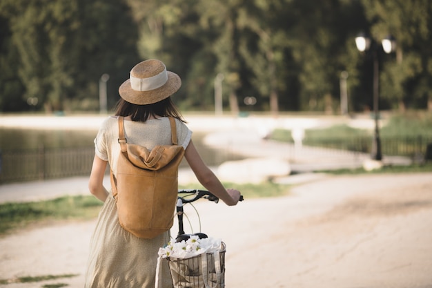 Porträt im Freien des attraktiven jungen Brunette in einem Hut auf einem Fahrrad.