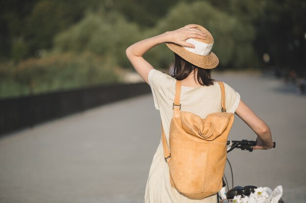 Porträt im Freien des attraktiven jungen Brunette in einem Hut auf einem Fahrrad.