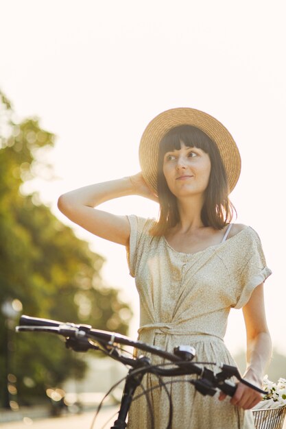 Porträt im Freien des attraktiven jungen Brunette in einem Hut auf einem Fahrrad.