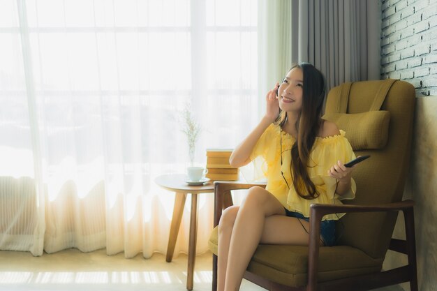 Porträt junge asiatische Frau sitzen auf Stuhl hören Musik mit Handy Kaffee und Buch