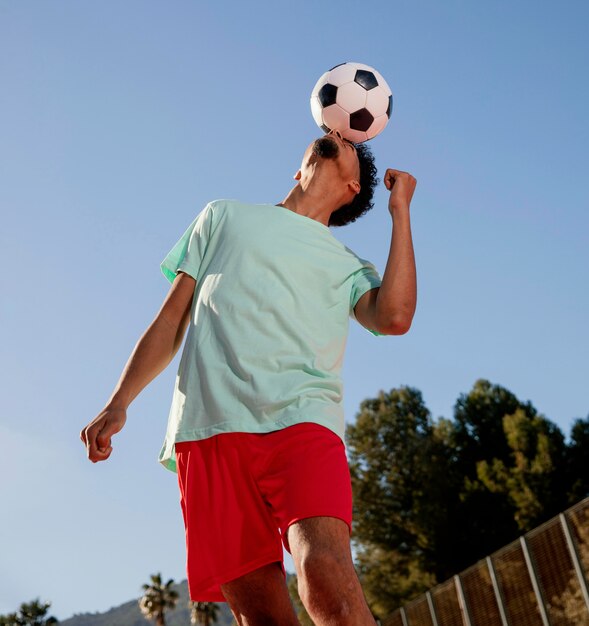 Porträt junger Mann, der Fußball mit Kopf spielt