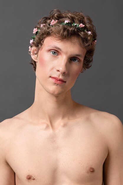 Porträt junger Mann, der Make-up und Blumenkranz trägt