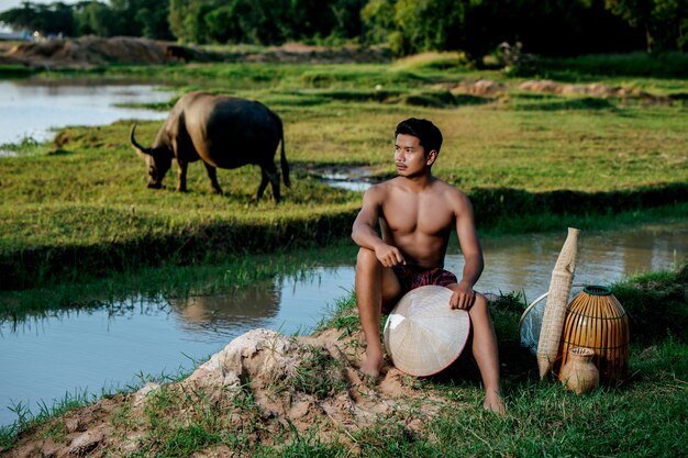 Porträt junger mann oben ohne in lendenschurz im ländlichen lebensstil sitzend mit bambus-fischerfalle Premium Fotos