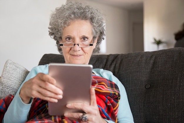 Porträt lächelnder alter Dame, die digitale Tablette im Wohnzimmer verwendet