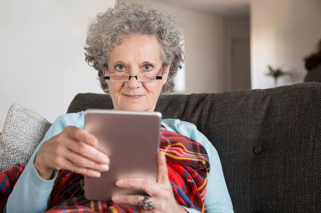 Porträt lächelnder alter Dame, die digitale Tablette im Wohnzimmer verwendet