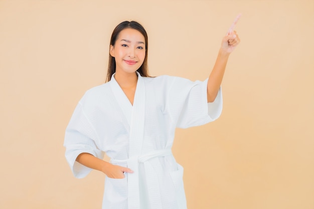 Porträt schöne junge asiatische Frau, die Bademantel mit Lächeln auf Beige trägt
