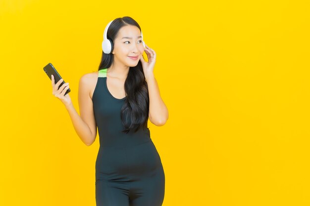 Porträt schöne junge asiatische Frau, die Turnhalle Outfit mit Kopfhörern und Smartphone trägt