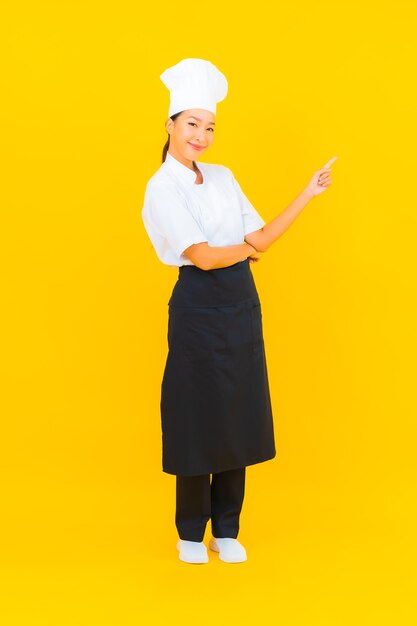 Porträt schöne junge asiatische Frau in Koch- oder Kochuniform mit Hut auf gelbem isoliertem Hintergrund