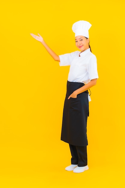 Porträt schöne junge asiatische Frau in Koch- oder Kochuniform mit Hut auf gelbem isoliertem Hintergrund