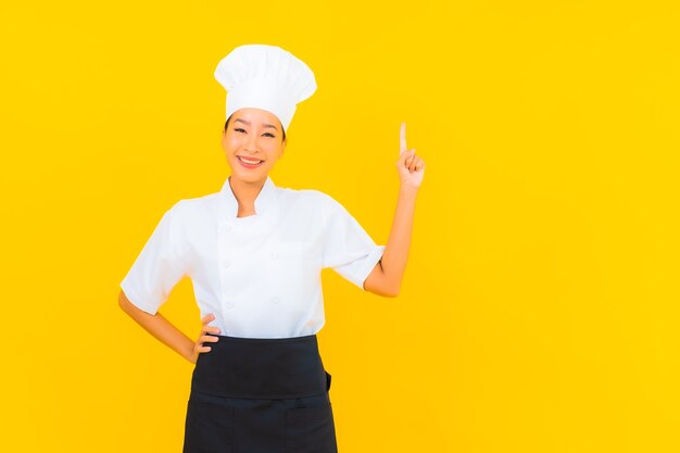 Porträt schöne junge asiatische Frau in Koch- oder Kochuniform mit Hut auf gelbem isoliertem Hintergrund