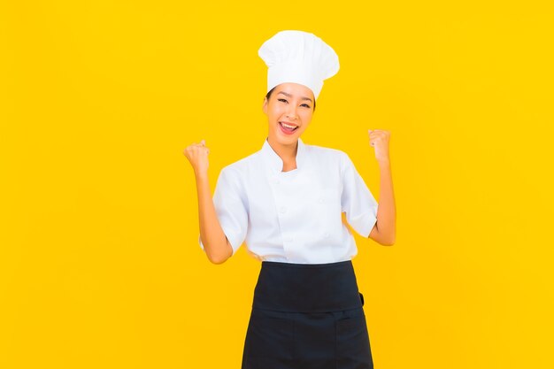 Porträt schöne junge asiatische Frau in Koch- oder Kochuniform mit Hut auf gelbem isoliertem Hintergrund