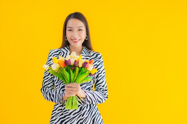Porträt schöne junge asiatische Frau lächeln glücklich mit Blume auf gelb