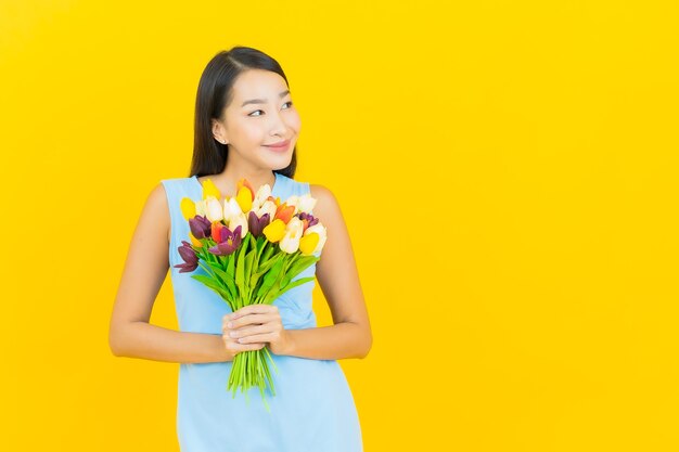 Porträt schöne junge asiatische Frau lächeln mit Blume auf gelber Farbwand