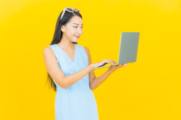 Porträt schöne junge asiatische Frau lächeln mit Computer Laptop auf gelbe isolierte Wand