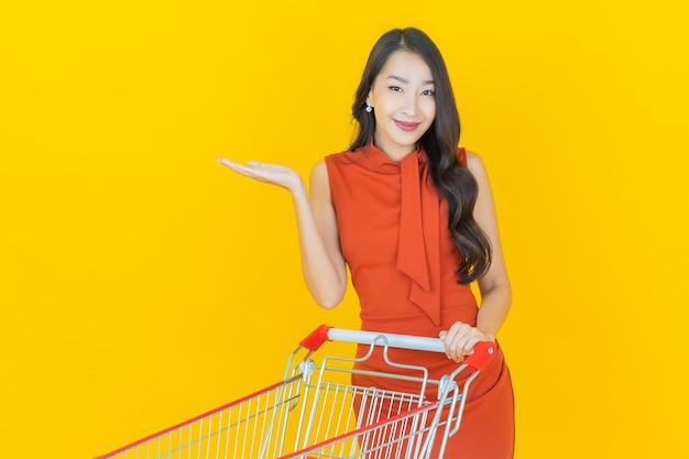 Kostenloses Foto porträt schöne junge asiatische frau lächeln mit einkaufskorb aus supermarkt auf gelb