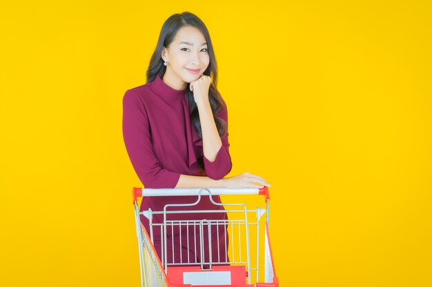 Porträt schöne junge asiatische Frau Lächeln mit Einkaufskorb aus Supermarkt auf Gelb