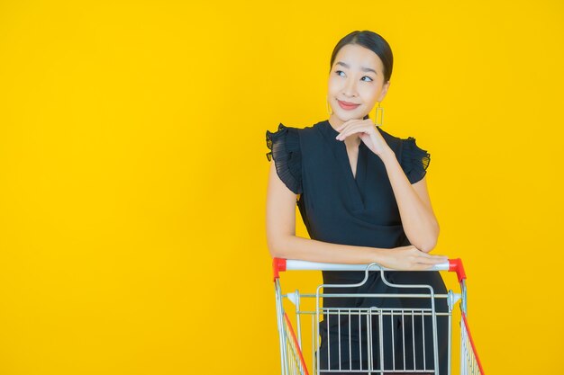 Porträt schöne junge asiatische Frau Lächeln mit Einkaufskorb vom Supermarkt auf Gelb
