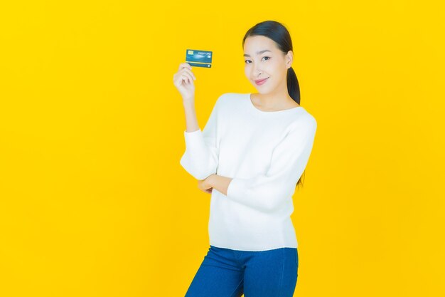 Porträt schöne junge asiatische Frau Lächeln mit Kreditkarte auf Gelb