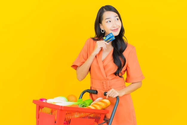 Porträt schöne junge asiatische Frau lächeln mit Lebensmittelkorb vom Supermarkt auf gelb