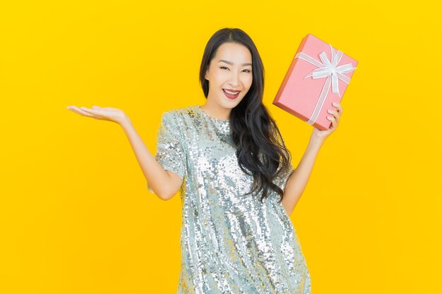Porträt schöne junge asiatische Frau lächeln mit roter Geschenkbox auf gelb