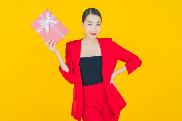 Porträt schöne junge asiatische Frau Lächeln mit roter Geschenkbox auf Gelb
