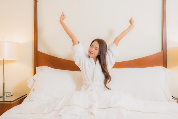 Porträt schöne junge asiatische Frau lächelt entspannend auf Bett im Schlafzimmer Interieur