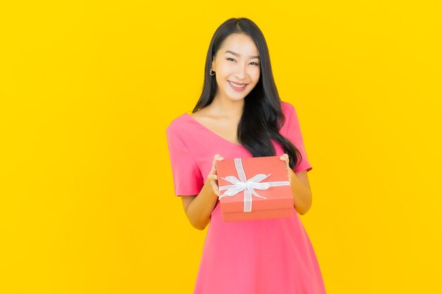 Porträt schöne junge asiatische Frau lächelt mit roter Geschenkbox auf gelber Wand