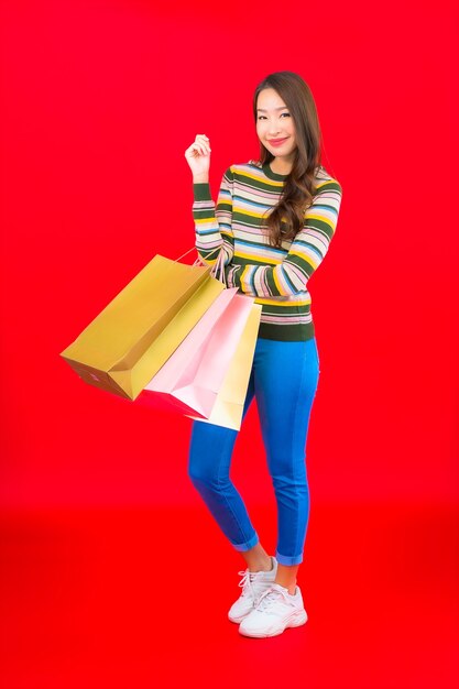 Porträt schöne junge asiatische Frau mit bunten Einkaufstaschen auf roter Wand