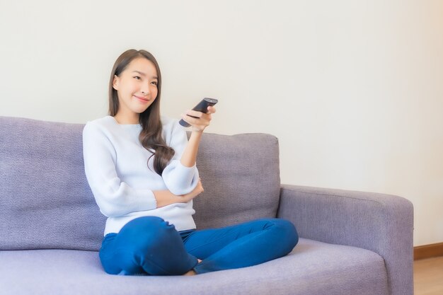 Porträt schöne junge asiatische frau mit fernbedienung für den kanalwechsel im fernsehen