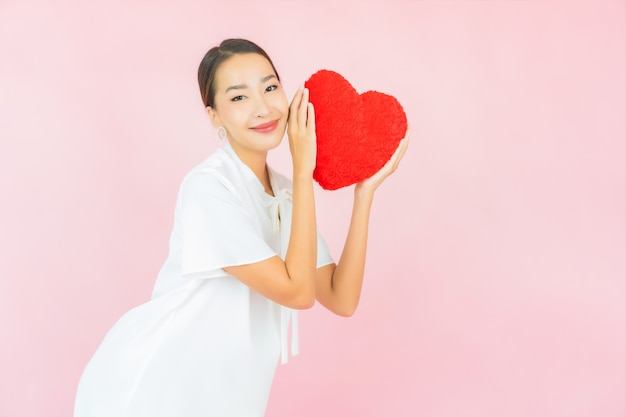 Porträt schöne junge asiatische Frau mit Herzkissenform auf rosa Wand