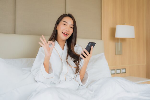 Porträt schöne junge asiatische Frau mit intelligentem Handy im Schlafzimmer
