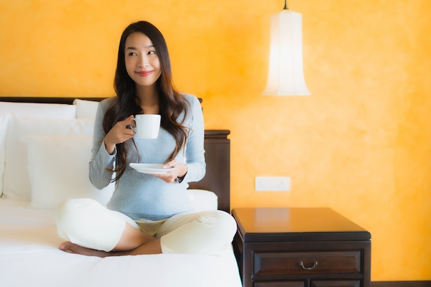 Porträt schöne junge asiatische Frau mit Kaffeetasse auf Bett im Schlafzimmer