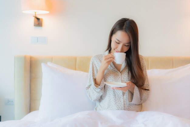 Porträt schöne junge asiatische Frau mit Kaffeetasse auf Bett
