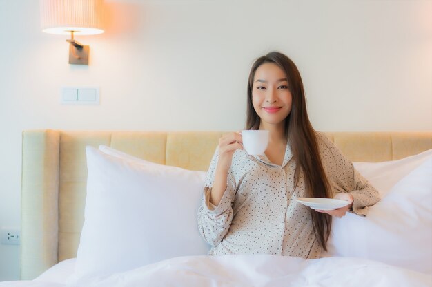 Porträt schöne junge asiatische Frau mit Kaffeetasse auf Bett
