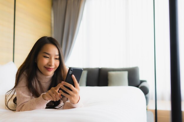 Porträt schöne junge asiatische Frau mit Kaffeetasse und Handy auf dem Bett