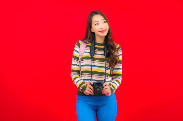 Porträt schöne junge asiatische Frau mit Kamerarucksack und Karte auf roter isolierter Wand