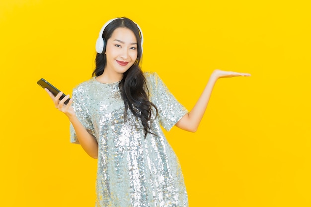 Porträt schöne junge asiatische Frau mit Kopfhörer und Smartphone für Musik auf gelb zu hören