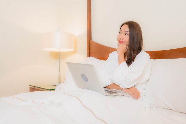 Porträt schöne junge asiatische Frau mit Laptop auf Bett im Schlafzimmer Interieur