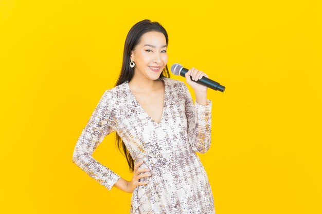 Porträt schöne junge asiatische frau mit mikrofon zum singen auf gelb