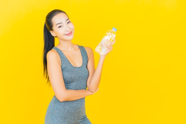 Porträt schöne junge asiatische Frau mit Sportbekleidung und Flaschenwasser auf gelber Wand