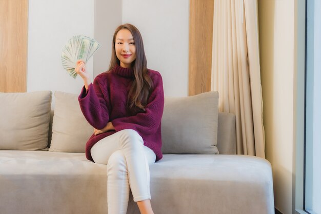 Porträt schöne junge asiatische Frau mit viel Geld und Geld auf Sofa im Wohnzimmer Interieur